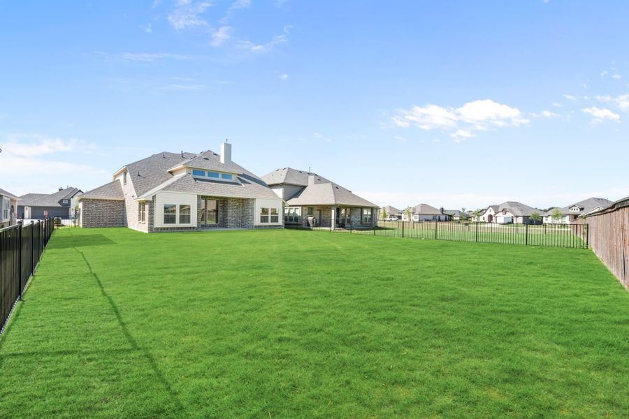 Brick home rear view with large fenced backyard, green lawn, and covered patio in a suburban neighborhood