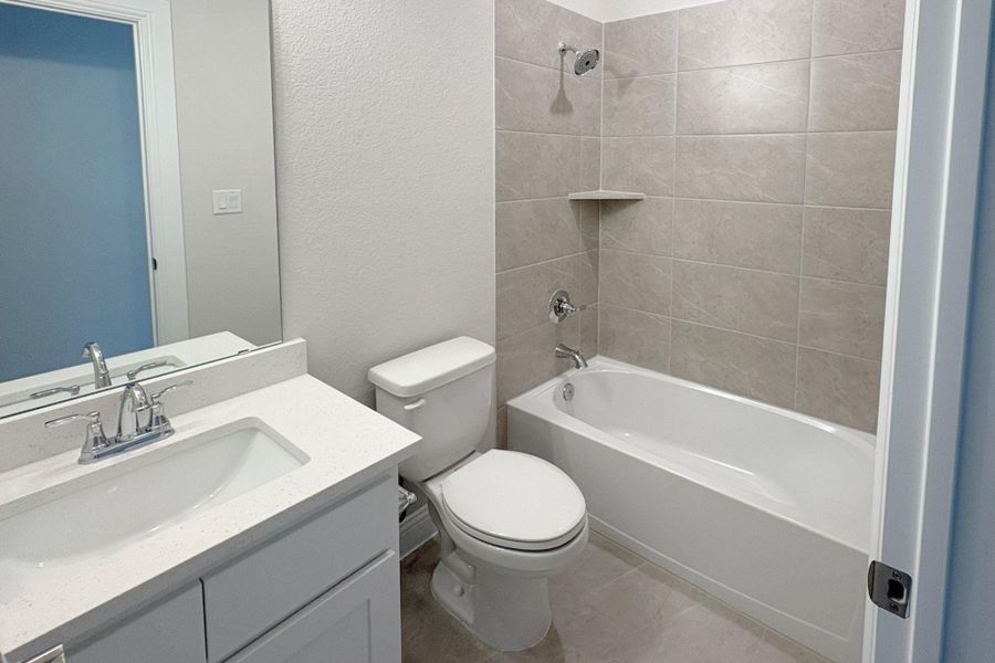 Bathroom featuring a single vanity with a white countertop and chrome faucet, a white toilet, and a bathtub with tiled surround