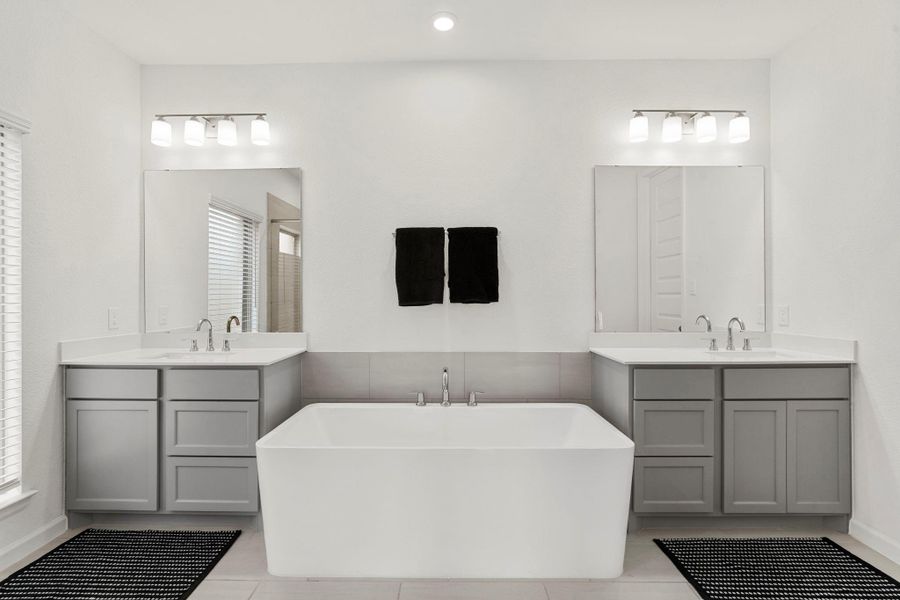 Luxurious primary bath with double sinks, gray cabinetry, and a modern freestanding soaking tub. Luxurious primary bath with double sinks, gray cabinetry, and a modern freestanding soaking tub.