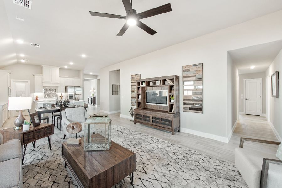 Open-concept living room with wood entertainment center, ceiling fan, and kitchen visible in background