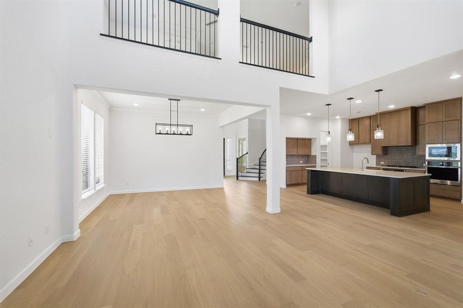 Open-concept living area with two-story ceilings, light wood-finish flooring, and crisp white walls