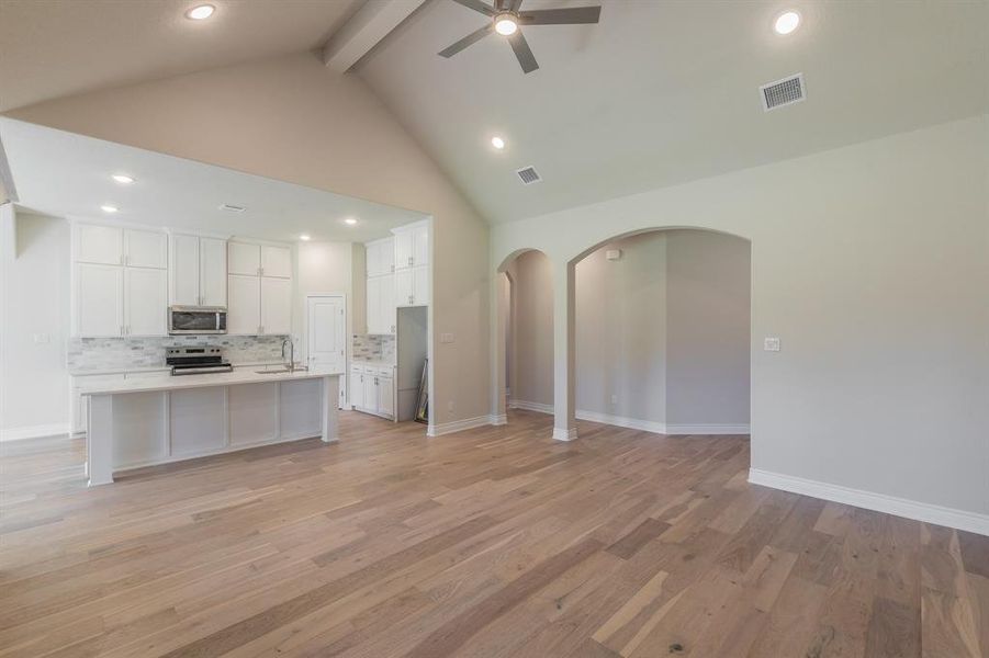 Kitchen with decorative backsplash, an island with sink, appliances with stainless steel finishes, light hardwood / wood-style floors, and white cabinetry