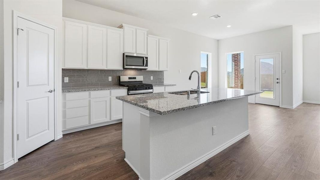 The kitchen features white cabinetry, a stainless steel microwave and stove, a gray tile backsplash, and granite countertops The kitchen features white cabinetry, a stainless steel microwave and stove, a gray tile backsplash, and granite countertops