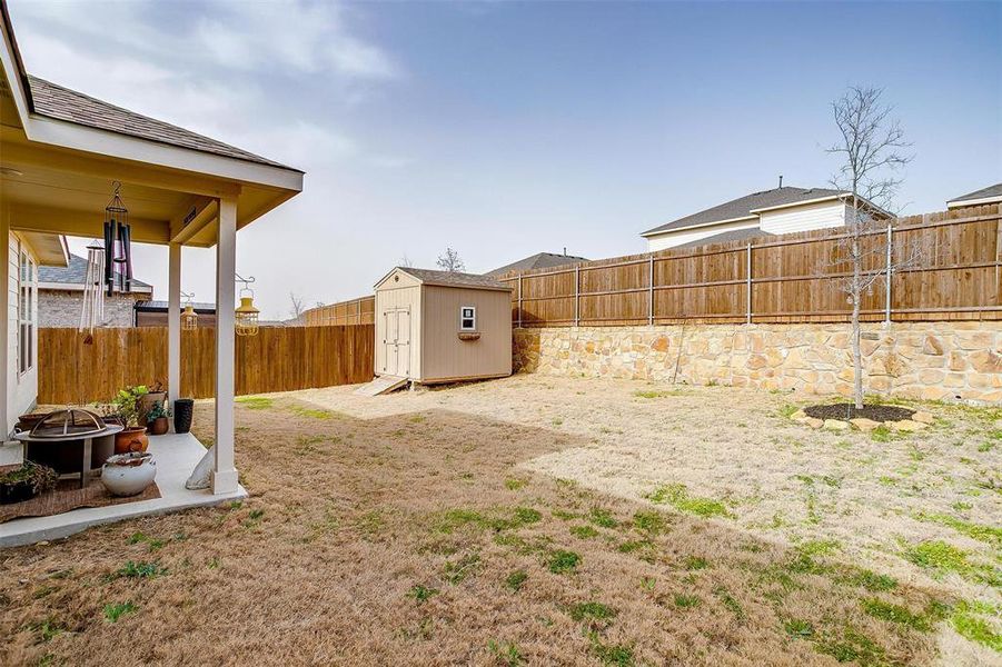 View of yard featuring an outbuilding, a patio, a storage unit, an outdoor fire pit, and a fenced backyard