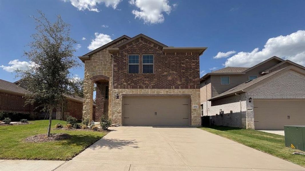 Two-story residence featuring a brick and stone facade, an arched entry, a two-car garage, and a concrete driveway Two-story residence featuring a brick and stone facade, an arched entry, a two-car garage, and a concrete driveway