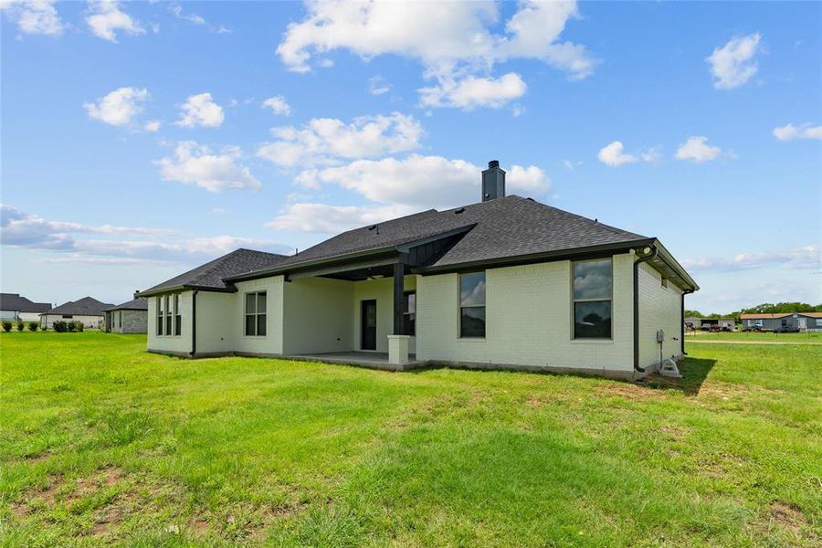Back of property with brick siding, a patio area, a shingled roof, a yard, and a chimney Back of property with brick siding, a patio area, a shingled roof, a yard, and a chimney