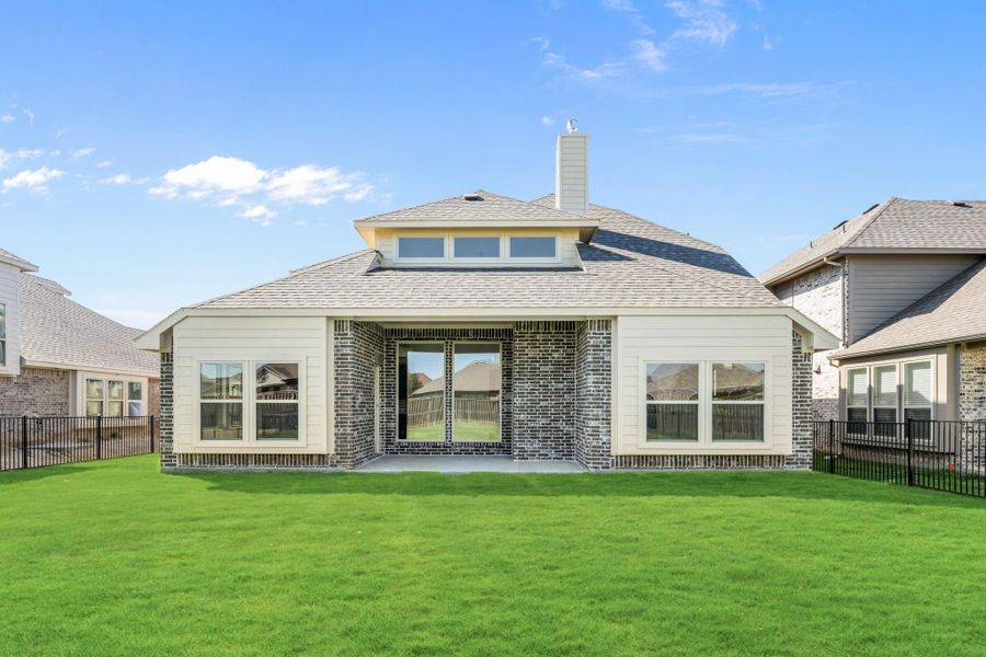 Rear exterior of single-story brick home with covered patio, chimney, and fenced backyard with green lawn