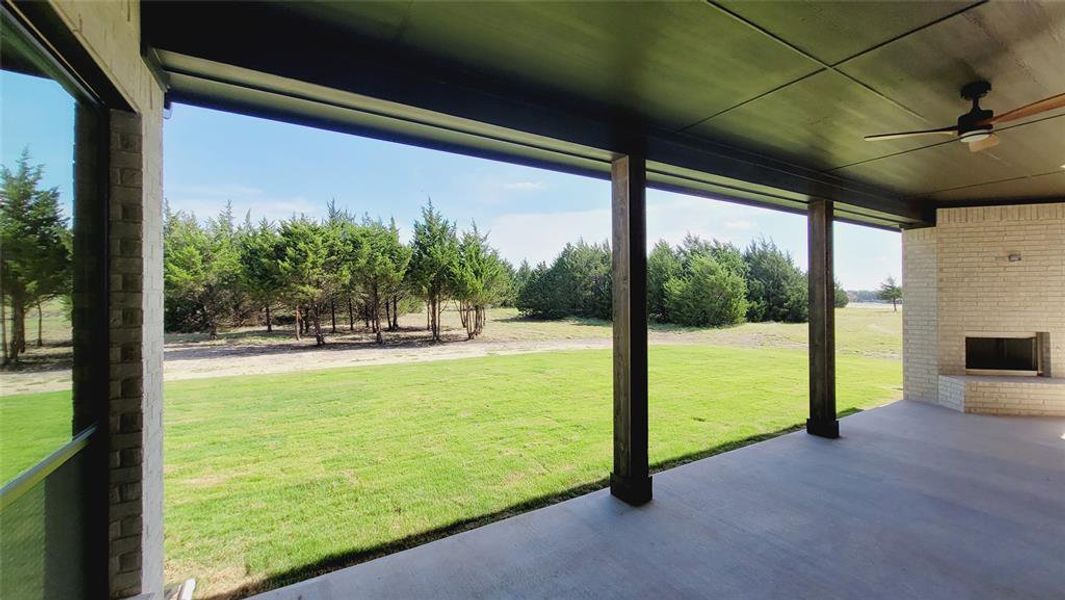 Covered patio featuring an outdoor fireplace with light brick surround, wood-finish columns, a ceiling fan, and concrete flooring