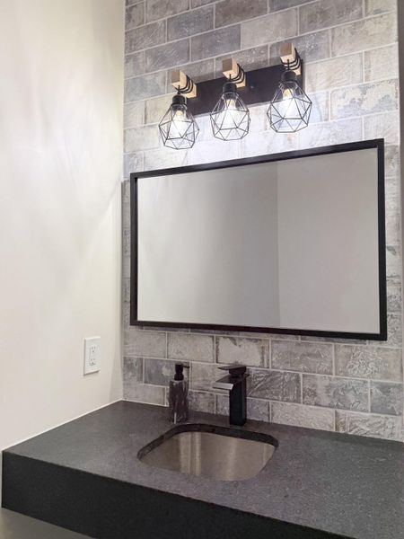 2nd Half Bath off back patio. Industrial style lighting illuminates a textured stone tile accent wall above the modern vanity.