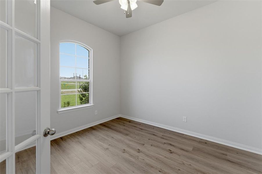 This bright room features a ceiling fan, a large arched window offering views of the outdoors, and light-toned flooring