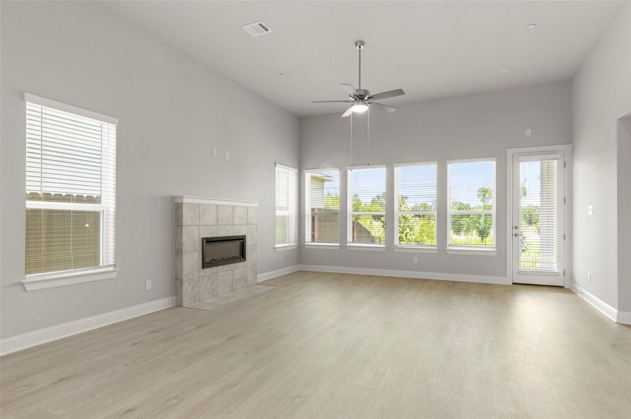 Unfurnished living room featuring light wood finished floors, a ceiling fan, plenty of natural light, and a tiled fireplace Unfurnished living room featuring light wood finished floors, a ceiling fan, plenty of natural light, and a tiled fireplace