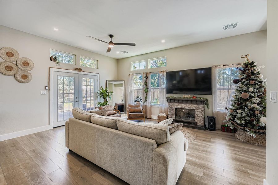 Living area featuring light wood-style flooring, a stone fireplace, french doors, recessed lighting, and ceiling fan Living area featuring light wood-style flooring, a stone fireplace, french doors, recessed lighting, and ceiling fan