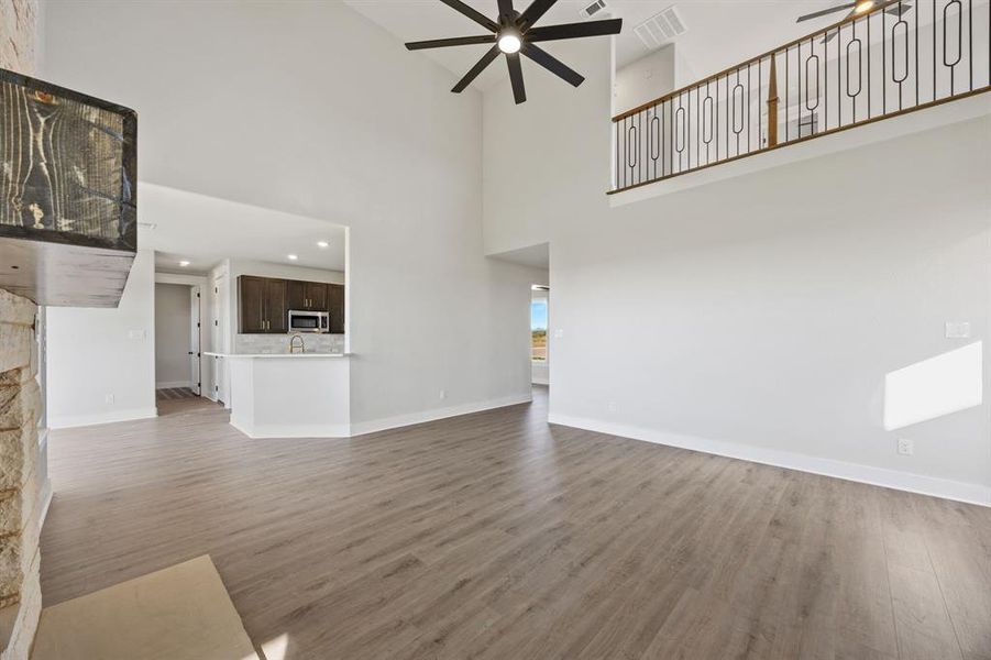 Unfurnished living room featuring a ceiling fan, wood finished floors, and a high ceiling
