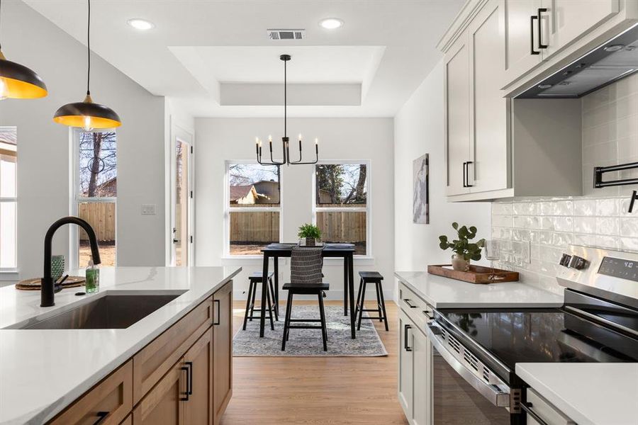 Kitchen featuring a sink, a tray ceiling, stainless steel electric stove, under cabinet range hood, and backsplash