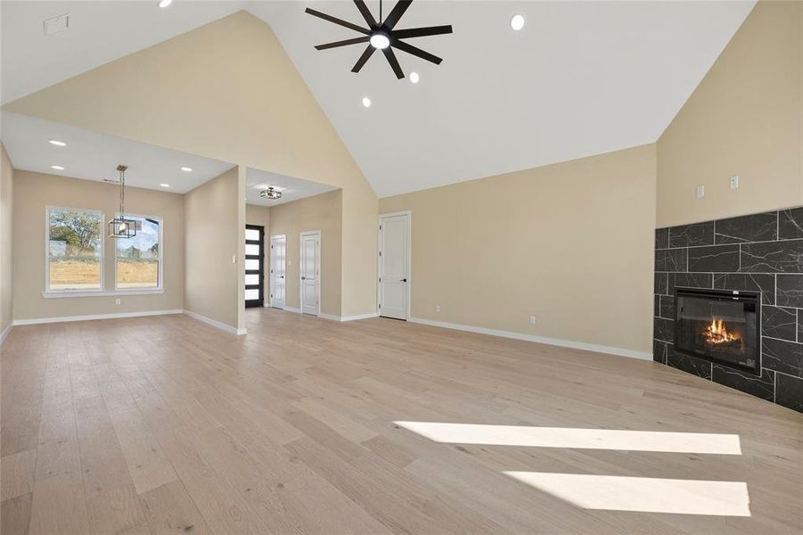 Unfurnished living room featuring ceiling fan with notable chandelier, high vaulted ceiling, light hardwood / wood-style flooring, and a fireplace