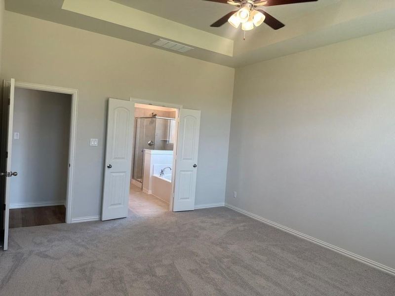 Carpeted room featuring a ceiling fan with light fixture, tray ceiling, and neutral wall tones Carpeted room featuring a ceiling fan with light fixture, tray ceiling, and neutral wall tones