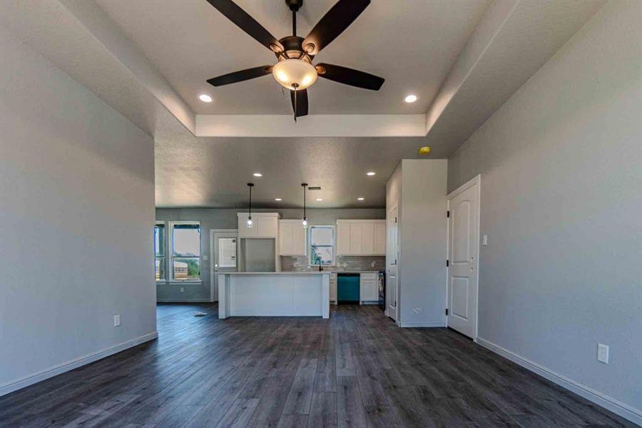 Unfurnished living room featuring recessed lighting, dark wood-style floors, a tray ceiling, and ceiling fan Unfurnished living room featuring recessed lighting, dark wood-style floors, a tray ceiling, and ceiling fan