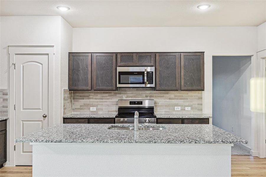 Kitchen with light stone counters, an island with sink, appliances with stainless steel finishes, and light hardwood / wood-style flooring