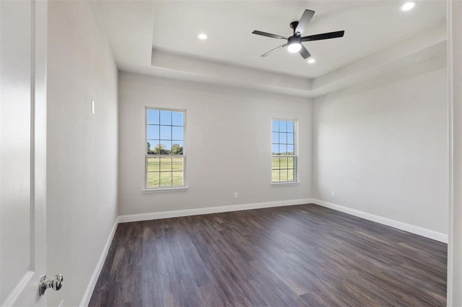 Empty room with ceiling fan, dark hardwood / wood-style flooring, and a tray ceiling