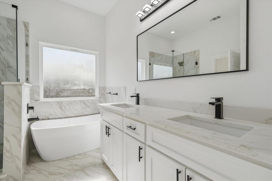 Primary Bathroom with light marble finish flooring, double vanity, a freestanding tub, a marble finish shower, and tile walls