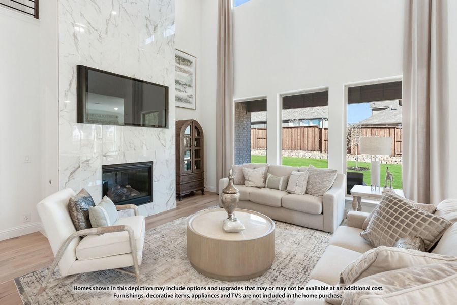 Living room with two-story ceiling, marble fireplace surround, wall-mounted TV, and large windows overlooking backyard Living room with two-story ceiling, marble fireplace surround, wall-mounted TV, and large windows overlooking backyard