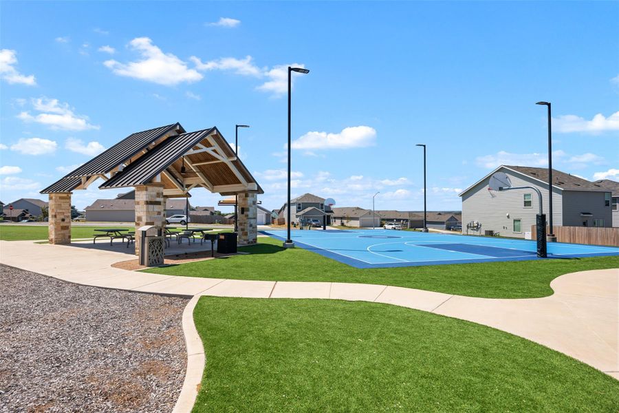 An outdoor community recreation area includes a covered picnic pavilion alongside a basketball court. An outdoor community recreation area includes a covered picnic pavilion alongside a basketball court.