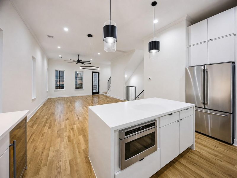 Another kitchen view highlights the spacious island, sleek white cabinetry, stainless steel appliances, and dramatic black pendant lighting. The open layout extends directly into the living and dining areas, creating a highly connected entertaining space. Warm wood flooring adds richness and continuity, while crisp countertops, modern hardware, and abundant cabinetry complete the refined contemporary design. Another kitchen view highlights the spacious island, sleek white cabinetry, stainless steel appliances, and dramatic black pendant lighting. The open layout extends directly into the living and dining areas, creating a highly connected entertaining space. Warm wood flooring adds richness and continuity, while crisp countertops, modern hardware, and abundant cabinetry complete the refined contemporary design.