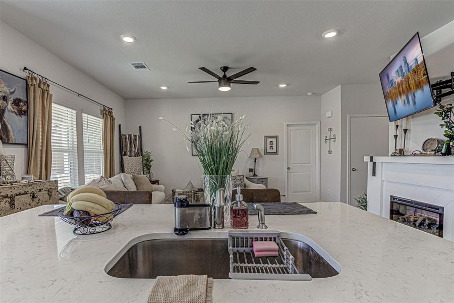 Kitchen with light stone counters, open floor plan, a glass covered fireplace, a ceiling fan, and recessed lighting