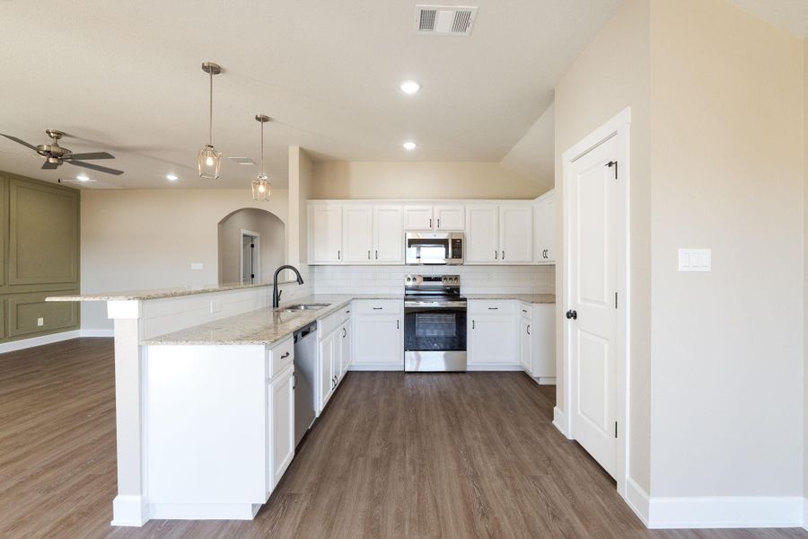 Kitchen with a peninsula, stainless steel appliances, decorative backsplash, pendant lighting, and dark wood finished floors