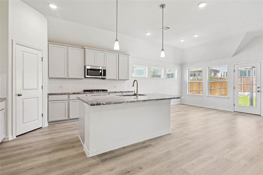 Kitchen featuring decorative backsplash, light hardwood / wood-style flooring, hanging light fixtures, an island with sink, and sink