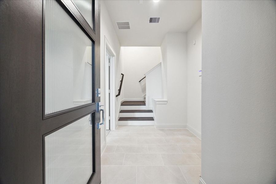 The inviting entryway of this modern home sets the tone for the stylish interiors. Clean tile flooring and an open layout create a bright and welcoming space. Just inside the entrance, you are greeted by a sleek staircase that leads to the main living areas and a first-floor bedroom, offering a harmonious flow between the floors. The design is minimal yet functional, providing a smooth transition from the outdoors into the home.