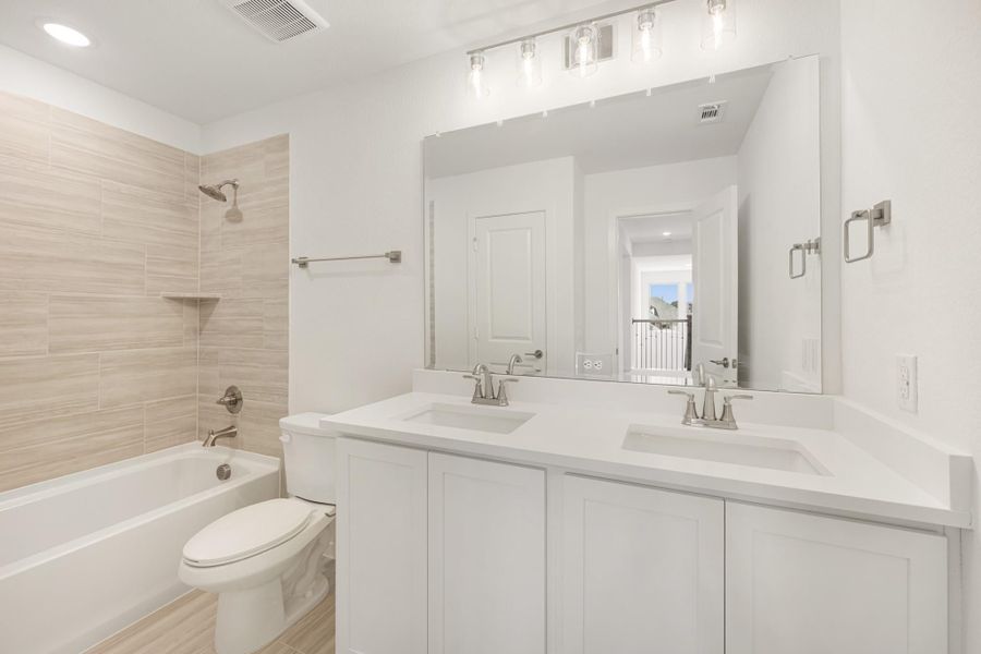 Bathroom with double sink vanity, white cabinets, large mirror, and tub-shower combo with beige tile walls