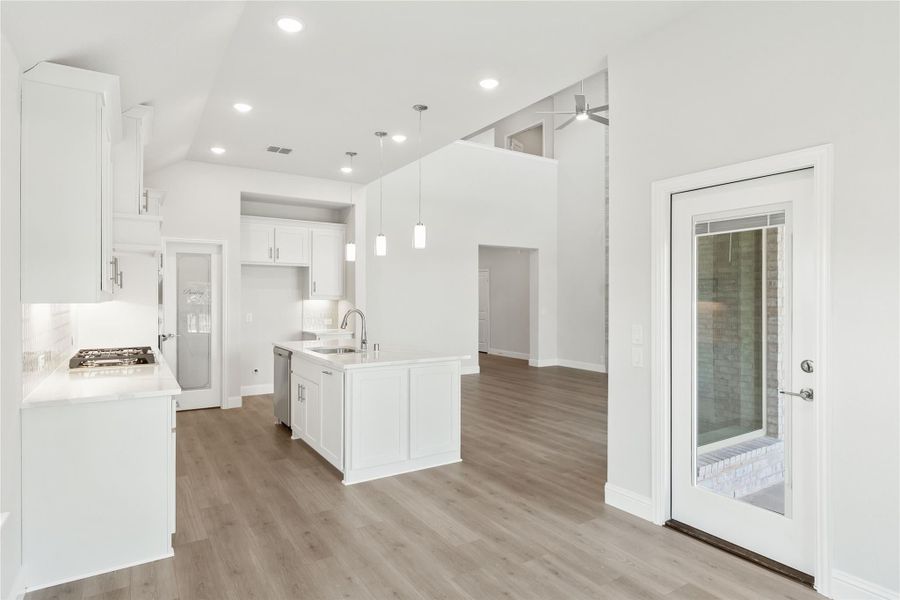 Open kitchen with white cabinets, center island, pendant lights, and wood floors leading to living area Open kitchen with white cabinets, center island, pendant lights, and wood floors leading to living area