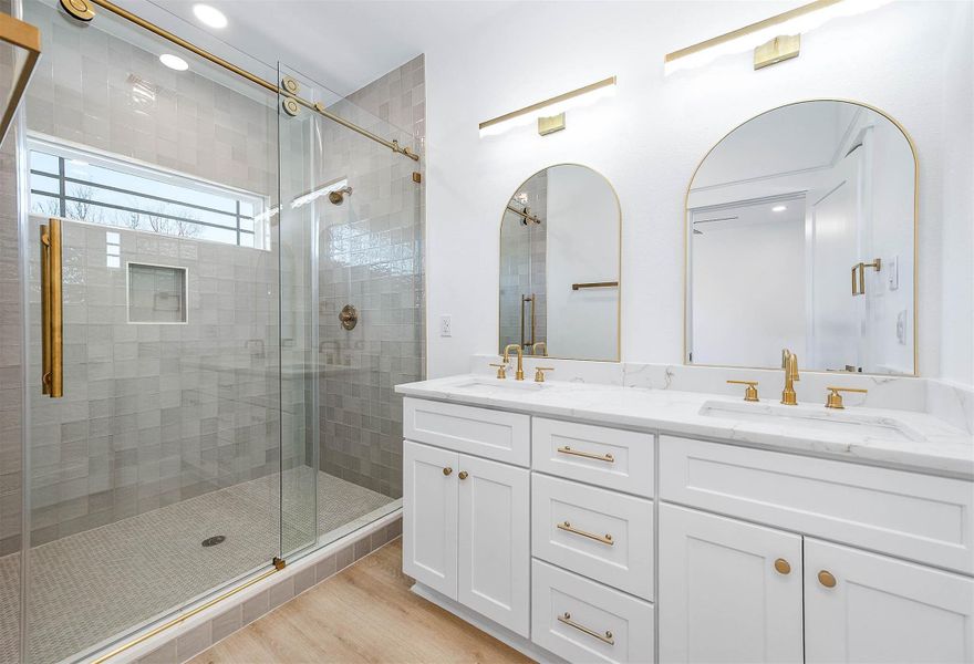Elegant bath with dual vanities and a sleek glass walk-in shower.
