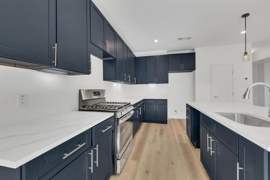 Kitchen featuring gas stove, light wood-type flooring, blue cabinets, light stone countertops, and pendant lighting