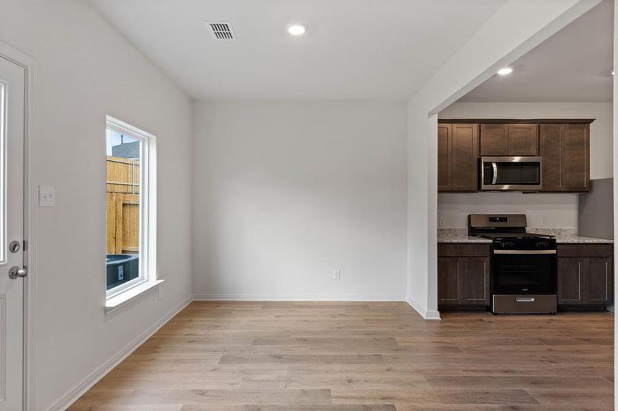 Kitchen with stainless steel appliances, light wood finished floors, dark brown cabinetry, recessed lighting, and light stone counters