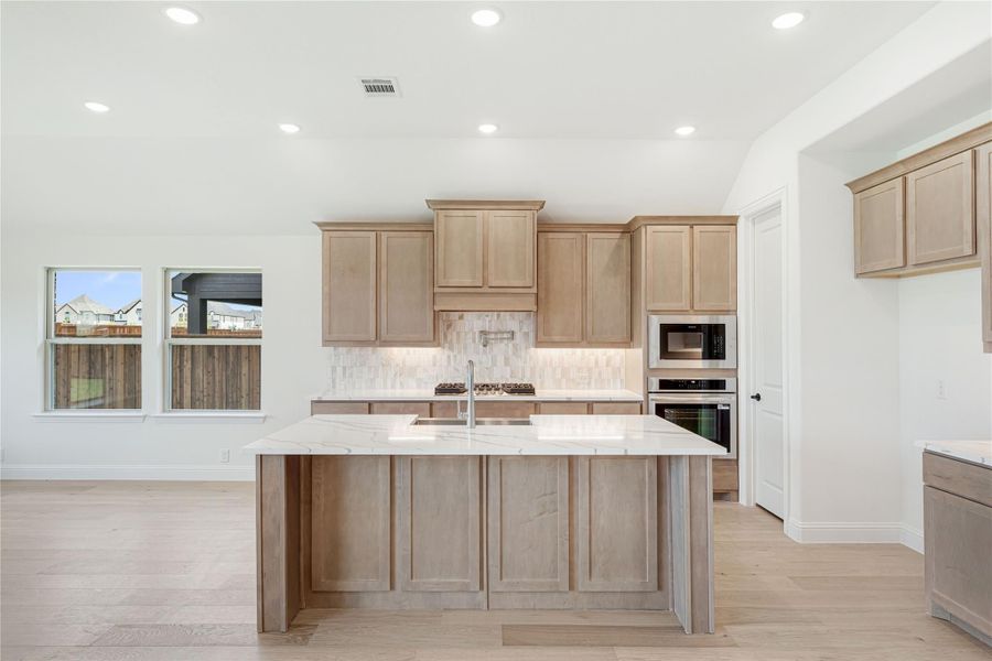 Kitchen with large center island, light wood cabinets, quartz countertops, and stainless steel appliances
