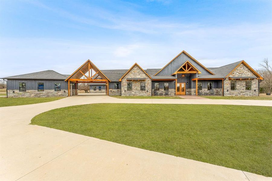 Modern farmhouse style home with stone siding, a front lawn, board and batten siding, and curved driveway