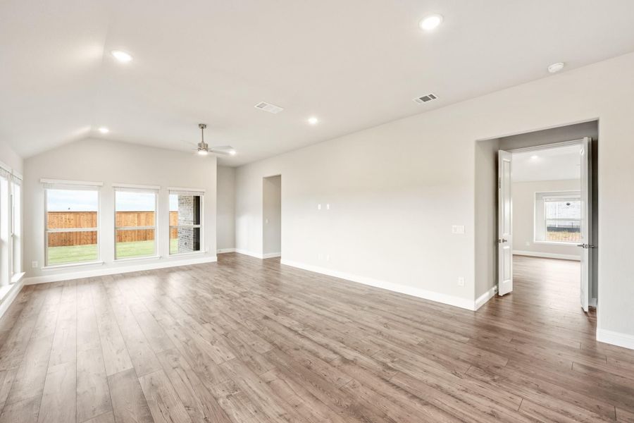 Open living room with vaulted ceiling, hardwood floors, and large windows overlooking backyard Open living room with vaulted ceiling, hardwood floors, and large windows overlooking backyard