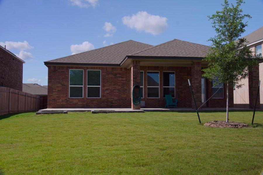 A vibrant green lawn extends from a spacious patio behind this charming brick residence.