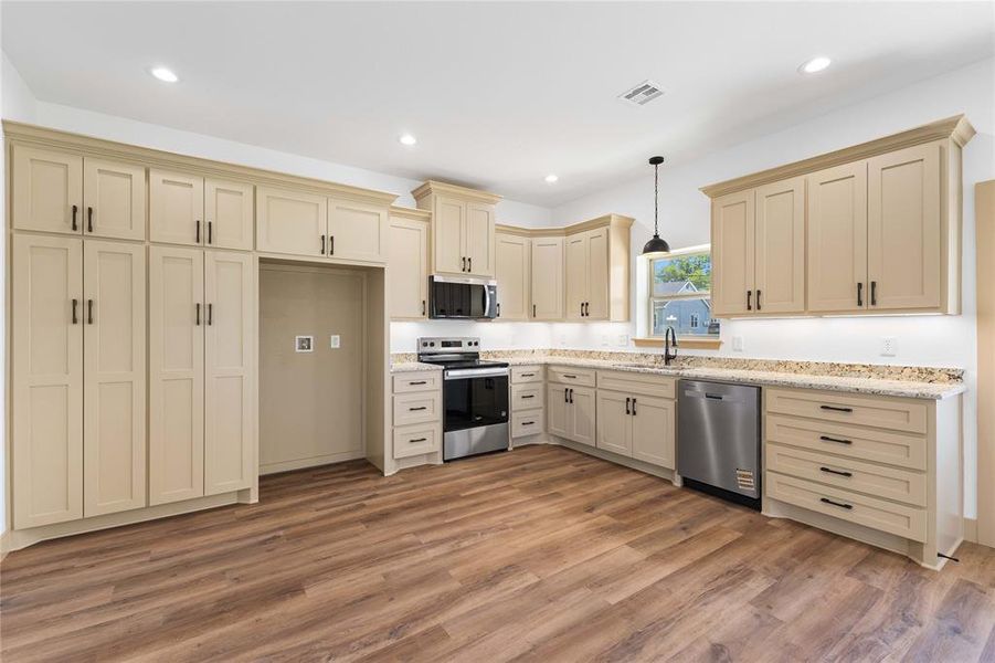 Kitchen featuring cream cabinets, appliances with stainless steel finishes, pendant lighting, light wood finished floors, and recessed lighting