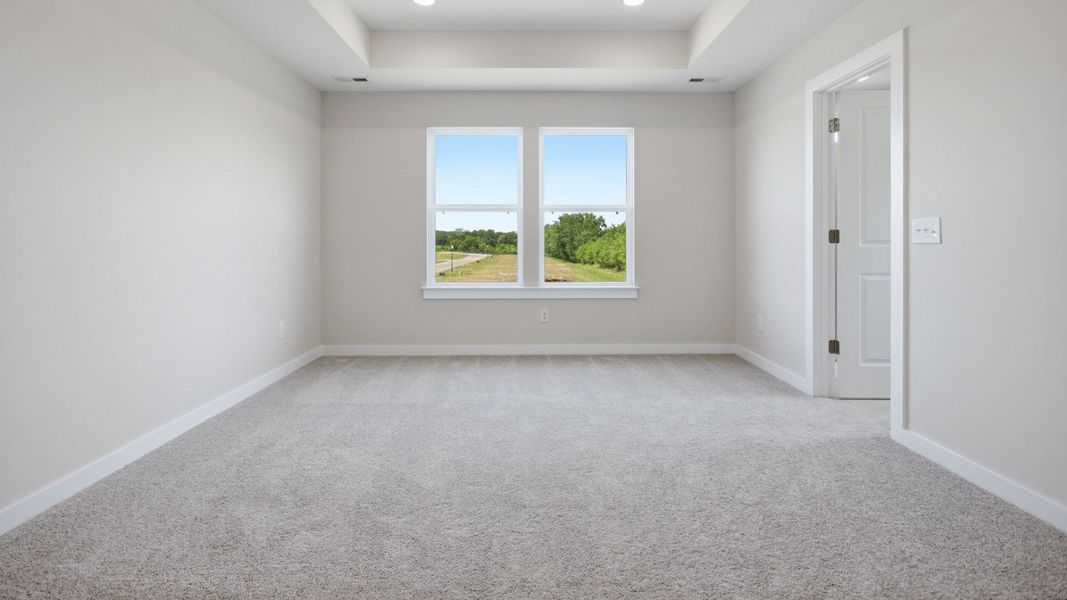 Bedroom with tray ceiling, windows, and entry to primary bathroom Bedroom with tray ceiling, windows, and entry to primary bathroom