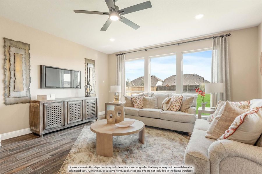 Living room with hardwood floors, ceiling fan, large windows, and neutral-toned sofas around a round wood coffee table Living room with hardwood floors, ceiling fan, large windows, and neutral-toned sofas around a round wood coffee table
