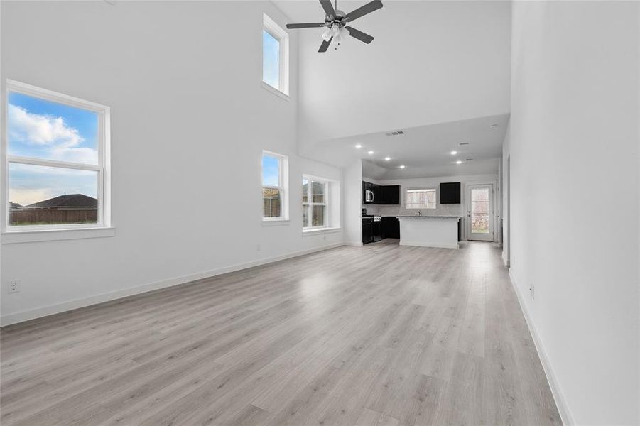 Unfurnished living room featuring a towering ceiling, light wood-style floors, and ceiling fan