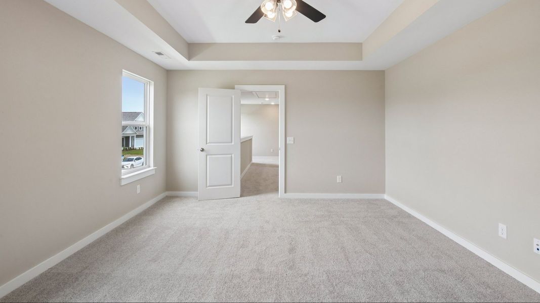 Bedroom with tray ceiling, windows, and entrance to primary bedroom