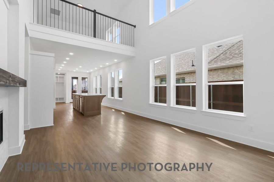 The family room features soaring ceilings and expansive windows, overlooking decorative balusters that connect it visually to the upstairs game room, creating an open and airy gathering space.
