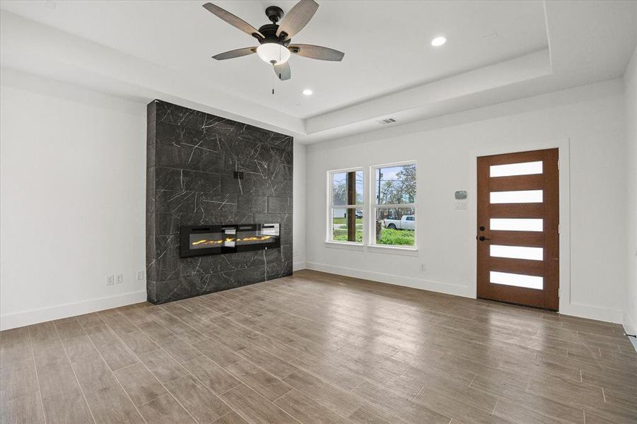 Unfurnished living room with wood tiled floors, a ceiling fan, a premium fireplace, recessed lighting, and a tray ceiling