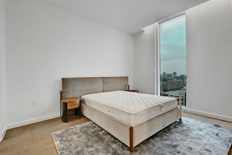 Step into this sleek and contemporary bedroom featuring floor-to-ceiling windows that frame spectacular views of the city and beyond. Furnishings provided by Scott + Cooner available for purchase separately. Photo is model unit #2406.