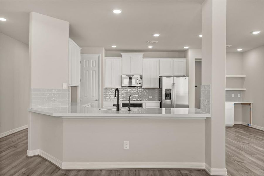 This light and bright kitchen features a large quartz island, white cabinets, a large sink overlooking your family room, recessed lighting, and beautiful backsplash.