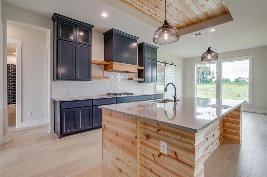 Kitchen featuring custom range hood, tasteful backsplash, wooden ceiling, an island with sink, and light wood-type flooring